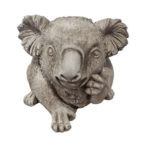 A realistic gray koala figurine sitting on a light wood surface against a plain light gray wall.