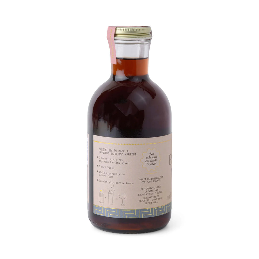 A bottle of Espresso Martini cocktail mixer by here's how, featuring a dark brown liquid in a ribbed glass bottle with a beige label and a gold cap, set against a light gray background.